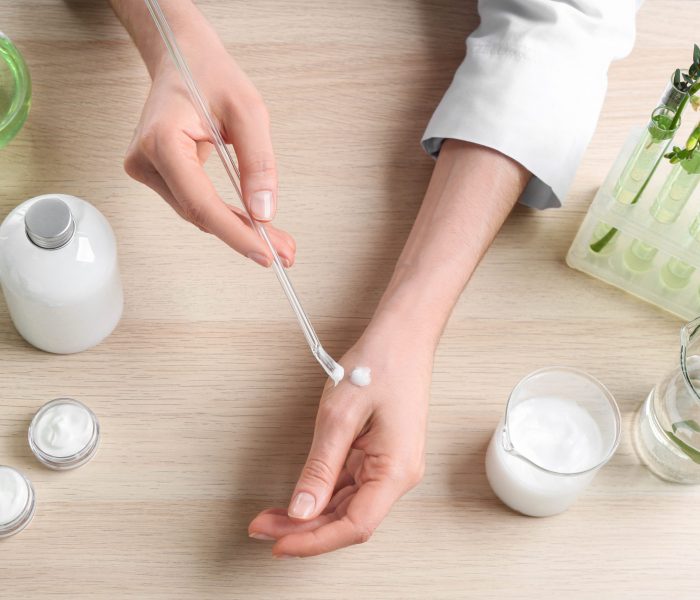 Woman applying natural cream onto hand in cosmetic laboratory, above view